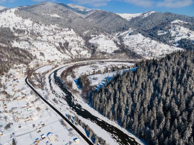 Soğuk dağlarda karla kaplı ormanlar arasında küçük köy evleri olan havadan kış manzarası 