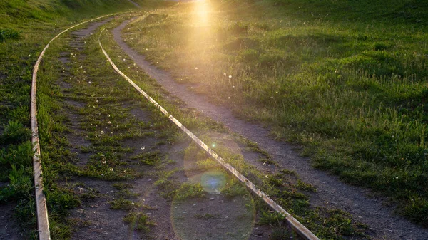 Viejas vías férreas en verano. Hay hierba verde alrededor. El sol brillante está brillando y el resplandor está en la parte inferior del marco. Vías ferroviarias curvas. — Foto de Stock