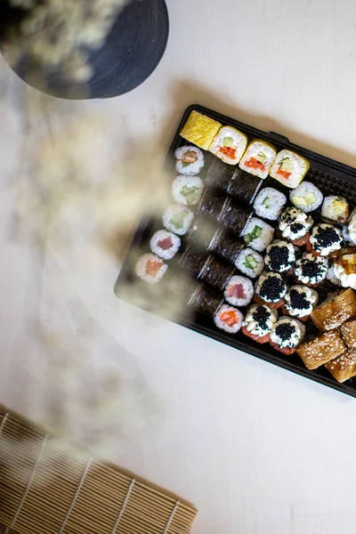 Sushi i bułki na stole. Wazon z suszonymi kwiatami. Wybiórcze skupienie. W pobliżu jest mata do robienia sushi. Robię sushi w domu. Zdrowe jedzenie. Widok góry. Sushi z rybą, serem wiejskim — Zdjęcie stockowe