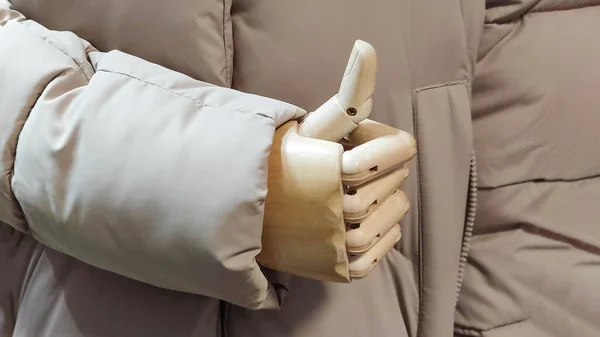 The wooden hand of a mannequin, a doll shows a thumbs-up gesture, super, positive concept. Wooden doll hand in a warm coat in store.
