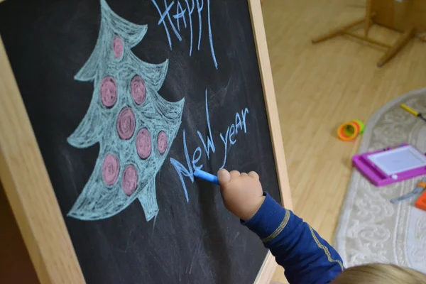 Надпись на доске "С Новым годом" и фигурка деревьев рядом и мальчик доросовывает руку — стоковое фото