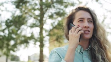 Kafkas 'lı genç bir kadının, yaz günü parkta ayakta dikilirken kahve içmek ve cep telefonuyla sohbet ederken görüntüsü.