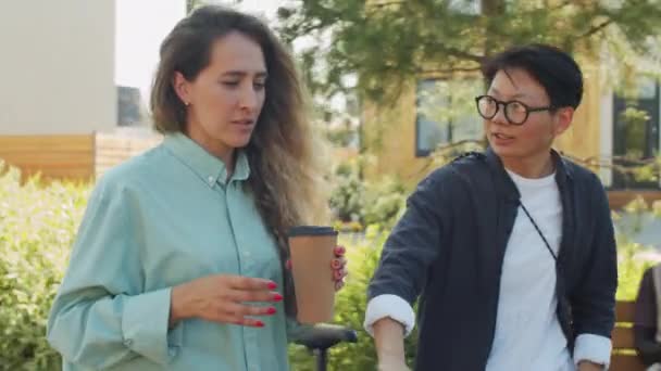 年轻的高加索女人抱着咖啡 与在公园骑自行车的亚洲女性朋友交谈 — 图库视频影像