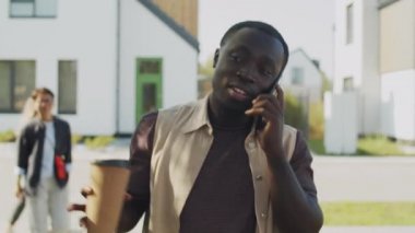 Sokakta yürüyen, kahve içen ve cep telefonuyla konuşan genç bir Afrikalı Amerikalı.