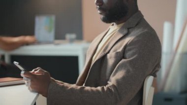 Yatay yan görüntü, şık giyinmiş yakışıklı Afro-Amerikan bir adamın akıllı telefondan mesaj attığı görüntüler.