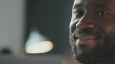 Yakından çekilmiş bir portre, yakışıklı Afro-Amerikan bir adamın kameraya gülümseyişini ve hafifçe başını sallayışını gösteriyor.