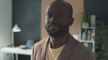 Yüzü sakallı, genç Afro-Amerikan bir adamın kameraya bakarken çekilmiş portresi.