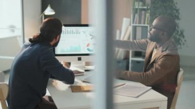 Yatay yüksek açı görüntüsü, modern ofiste finans stratejisi üzerinde çalışan iki genç Afrikalı ve Ortadoğulu adamın görüntülerini çekti.