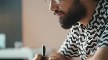 Yatay yan görüntü. Gözlüklü yakışıklı bir gencin not defterine bir şeyler yazarken çekilmiş görüntüleri.