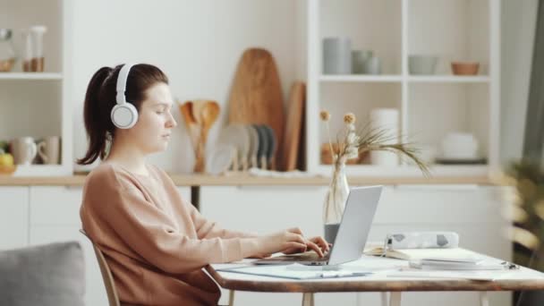 Mujer Morena Joven Auriculares Inalámbricos Sentados Mesa Escribiendo Ordenador Portátil — Vídeos de Stock