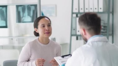 Güzel melez kadın kliniğe giriyor, erkek doktora tıbbi geçmiş veriyor, onunla konuşurken gülümsüyor ve danışmanlık yapıyor.