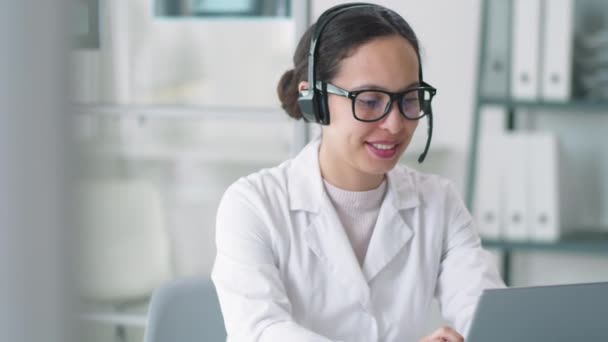 Junge Schöne Ärztin Labormantel Brille Und Drahtlosem Headset Mit Laptop — Stockvideo