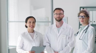 Profesyonel erkek doktor ekibi ve laboratuvar önlüklü iki kadın doktor kamera önünde birbirlerine poz veriyorlar ve gülümsüyorlar.