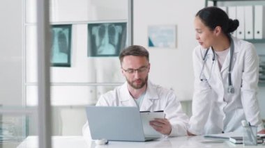 Profesyonel erkek doktor, kadın asistanla konuşuyor. Sonra neşeli meslektaşlar kameraya bakıp gülümsüyor.
