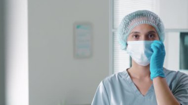 Tek kullanımlık şapkalı ve önlüklü güzel kadın hemşirenin koruyucu maskeyi çıkartıp kameraya özgüvenle baktığı göğüs görüntülerini göster. Covid-19 salgın konsepti