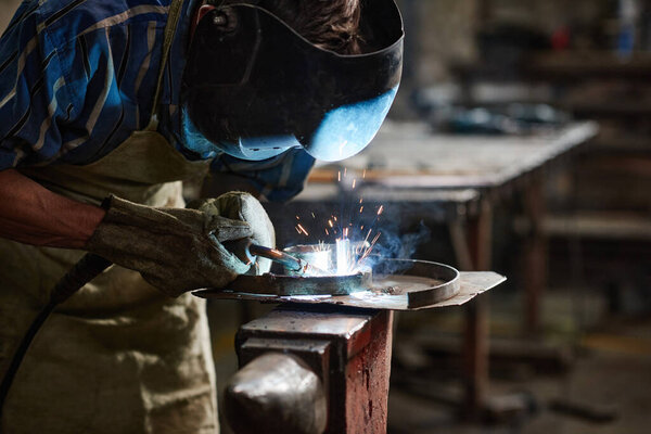 Close-up of worker in protective mask using welding to work with metal in the factory
