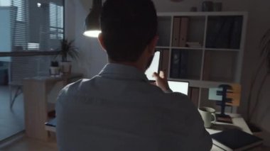 Resmi kıyafet ve gözlüklü yakışıklı Arap işadamının ofis masasında otururken gülümseyip mesajlaştığı 360 derecelik bir çekim.
