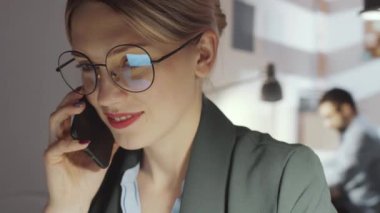 Ofiste geç saatlere kadar çalışırken, gözlüklü, gülümseyen ve telefonda konuşan güzel sarışın iş kadınının 360 derecelik izleme görüntüsünü kapat.
