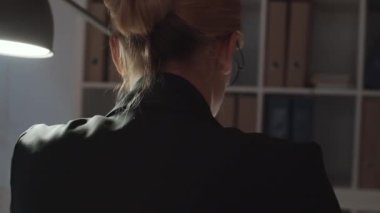 Genç beyaz iş kadınının bilgisayarda yazı yazarken, gözlüğünü çıkarırken ve karanlık ofiste geç saatlere kadar çalışmaktan yorulurken burnunun köprüsünü ovalarken göğsünü 360 derecelik açıyla izleme görüntüsü.