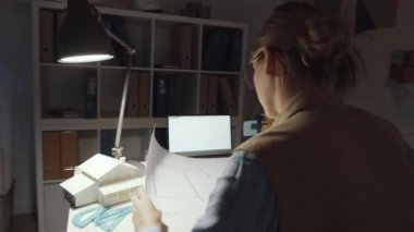 Beyaz kadın mimarın ofiste yürürken, masada otururken, kağıt sararken ve gece çalışırken kalem ve cetvelle inşaat planı çizerken 360 derecelik bir izleme görüntüsü.