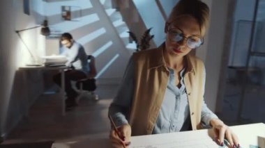 360 derecelik güzel kadın mimarın kalem kullanıp kare çizerken karanlık ofisteki masanın üzerine bina planını çizdiğini gösteren bir kare.
