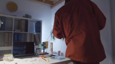 Ortadoğulu genç erkek tasarımcının akıllı telefonuyla yazı yazarken, raflarda giysileri kontrol ederken ve geç saatlere kadar moda stüdyosunda çalışırken masa başında otururken 360 derecelik bir izleme görüntüsü.