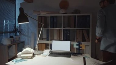 Ortadoğulu erkek mimarın masa başında dizüstü bilgisayarda yazarken 360 derecelik bir izleme görüntüsü, sonra raflara doğru yürürken, gece ofiste çalışırken dosyaları ve belgeleri okurken.