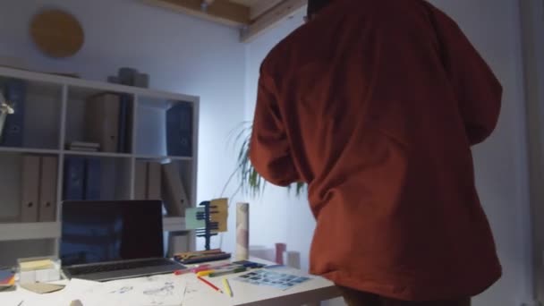 360度追踪照片 年轻的中东男性设计师在智能手机上打字 检查衣架上的衣服 在时尚工作室工作到很晚的时候坐在办公桌前 — 图库视频影像