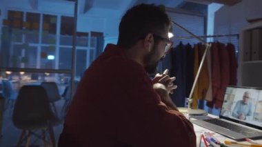 Moda stüdyosunda geç saatlere kadar çalışırken iş arkadaşlarıyla internet üzerinden konuşan, kablosuz kulaklıklı genç erkek tasarımcının 360 derecelik görüntüsü.
