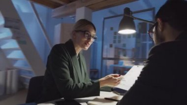 Genç sarışın iş kadınının, gece ofiste birlikte çalışırken panodaki belgeyi erkek ortadoğulu iş arkadaşına açıklarken 360 derecelik bir izleme görüntüsü.