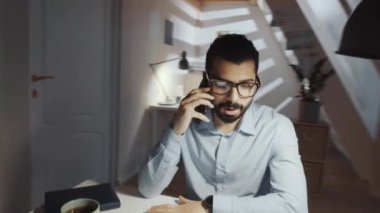 Resmi giyimli ve gözlüklü profesyonel Orta Doğulu iş adamının ofiste otururken cep telefonuyla konuşurken 360 derecelik izleme görüntüsü.