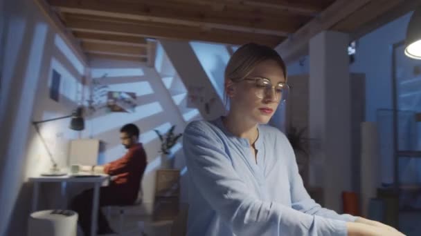 360度的跟踪镜头 漂亮的女设计师晚上在时尚工作室工作时 戴着无线耳机 在办公桌前听智能手机上的音乐 — 图库视频影像