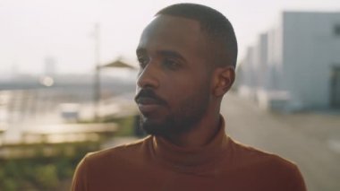 Genç Afrikalı Amerikalı adamın göğüs portresi. Sokakta dikilip kameraya bakıyor ve gülümsüyor.