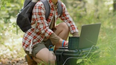 Genç Asyalı bir kadının taşınabilir mini güneş paneli kullanarak yerel bir ormanda dizüstü bilgisayarda çalışırken ki görüntülerini kaldır.