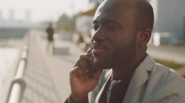 Resmi takım elbiseli Afro-Amerikan işadamının görüntülerini yukarı kaldır. Elinde kahve içmek ve cep telefonuyla kentteki barajın önünde dikilirken.