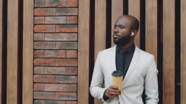 Resmi takım elbiseli, kablosuz kulaklıklı, elinde tek kullanımlık kahve fincanı olan ve kameraya poz veren Afro-Amerikan işadamlarının belden yukarısını çek.