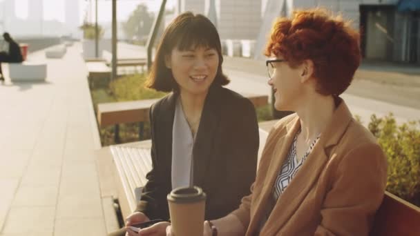 Young Asian Caucasian Businesswomen Sitting Together Bench Street Holding Coffee — Stock Video