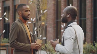 İki Afro-Amerikalı iş adamı, ellerinde kahve fincanları ile şehirde dikilip bir şeyler tartışıyorlar.