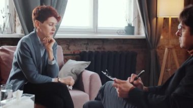 Mutsuz kadın kanepede oturuyor ve terapi sırasında bazı notlar yazan erkek psikologlara sorunlarını anlatıyor.