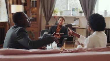 Duygusal Afrikalı Amerikalı çift koltukta oturup tartışırken Kafkas erkek psikolog terapi seansı boyunca onları dinliyor.