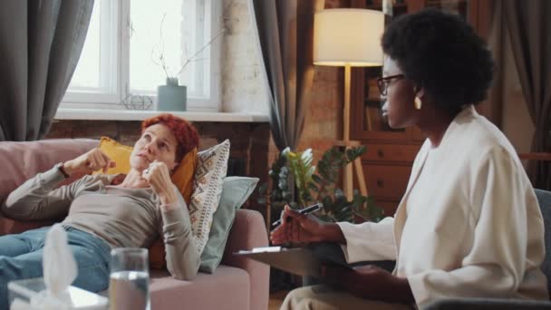 うつ病の白人女性はソファに横になり 治療セッション中にアフリカ系アメリカ人女性心理学者の質問に答える — ストック動画