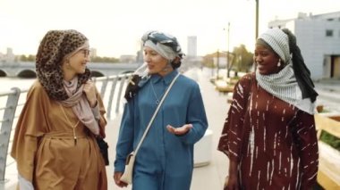 Üç etnik çeşitliliğe sahip Müslüman kadının gündüz vakti sette yürümesi, arkadaşlarının sohbet etmesi ve gülümsemesi.