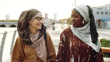 Siyahi ve Ortadoğulu Müslüman kadınların gündüz vakti sette yürüdüğü, arkadaşlarının konuştuğu ve gülümsediği bir ortam.