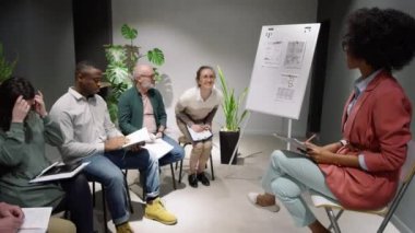Afro-Amerikan kadın iş koçu genç beyaz meslektaşını seyircilerle tanıştırıyor. Pozitif kadın ayağa kalkıyor, gülümsüyor ve çeşitli çalışanlardan oluşan bir takıma sunum yapıyor.