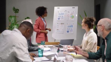 Güzel Afro-Amerikalı iş kadını, finansal şemalar çiziyor ve ofisteki takım toplantısında karışık yaş çok ırklı meslektaşlarına iş sunumu yapıyor.