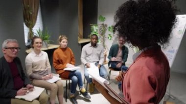 Güzel Afro-Amerikan kadın iş koçu karışık yaştaki çalışanların önünde duruyor ve seminer odasında konferans veriyor.