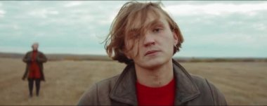 Sonbahar sahasında dikilip kameraya bakan genç bir adamın portresi.