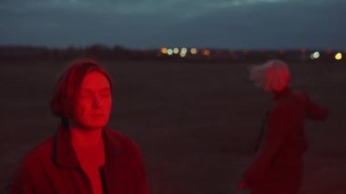 Genç adam dışarıda kırmızı ışıkta müzik dinlerken, arkada dans eden kaygısız kadın.