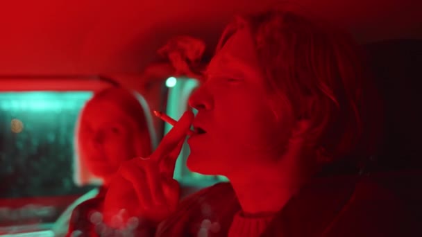 Молодой Человек Женщина Сидят Машине Красным Неоновым Светом Курят Сигареты — стоковое видео