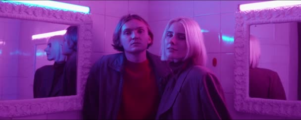 Portrait of young stylish couple standing between two mirrors in room filled with purple neon light and posing for camera — Stock Footage Portrait Young Stylish Couple Standing Two Mirrors Room Filled Purple — Stock Video